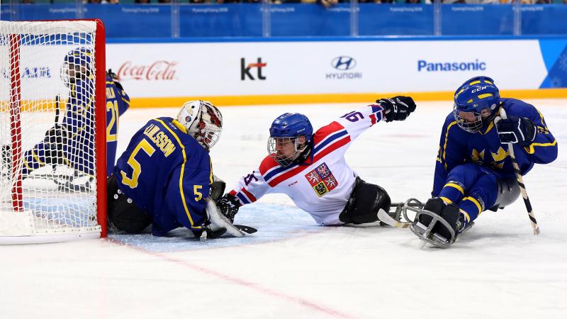 three ice hockey players clash in front of goal