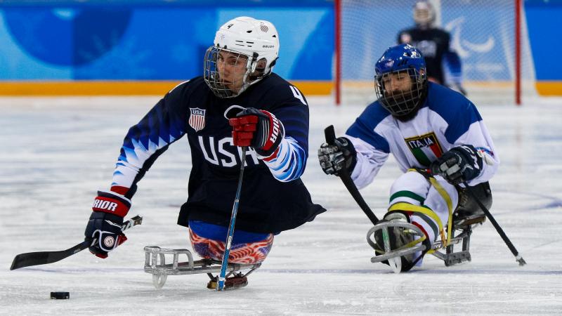 Two athletes on sledges playing Para ice hockey