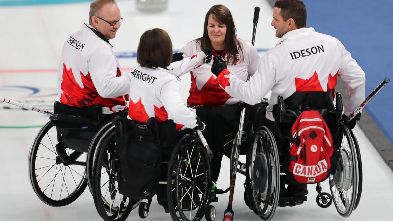 four wheelchair curlers gather in a huddle