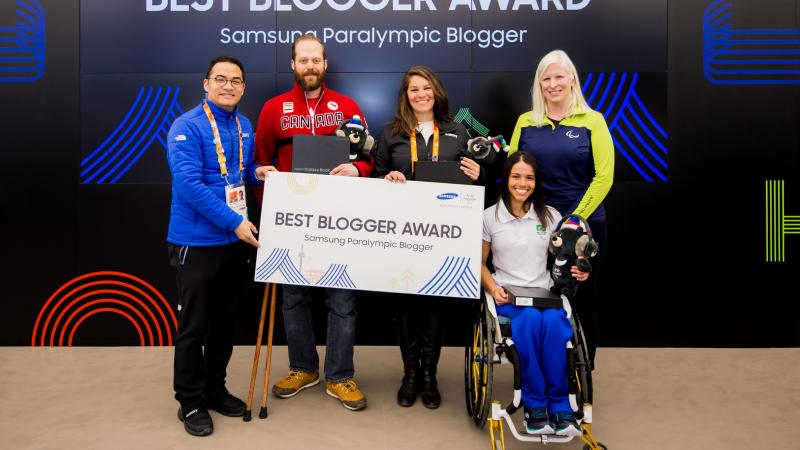 five people standing in front of a video screen