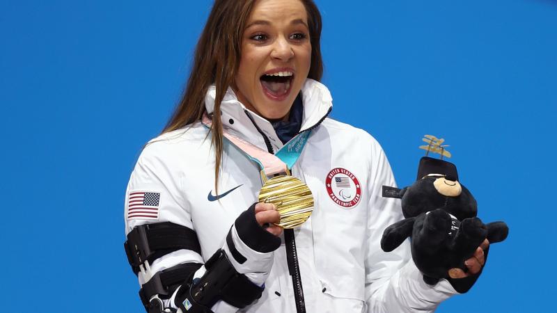 a female Para athlete holds up her gold medal and her mascot