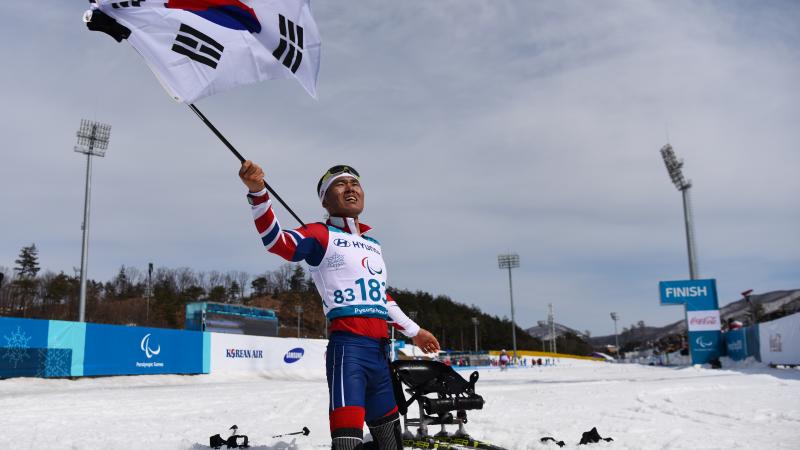 a male Para Nordic skier celebrates with the South Korean flag