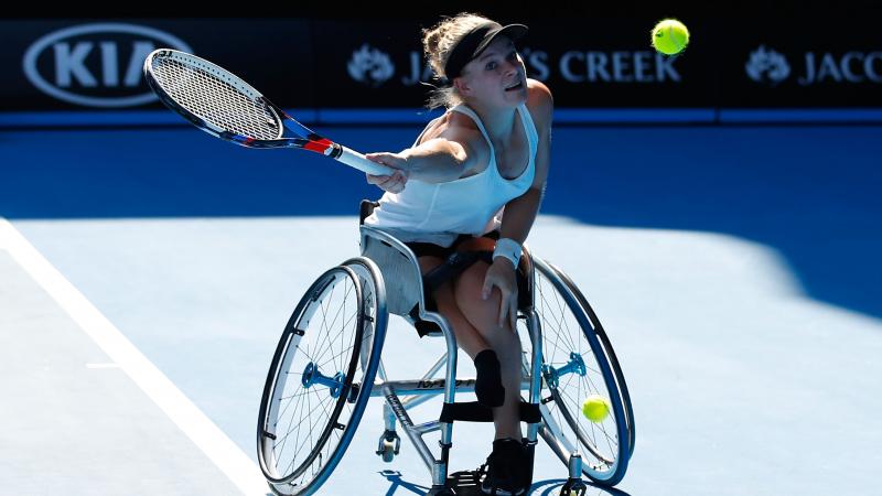 a female wheelchair tennis player makes a shot