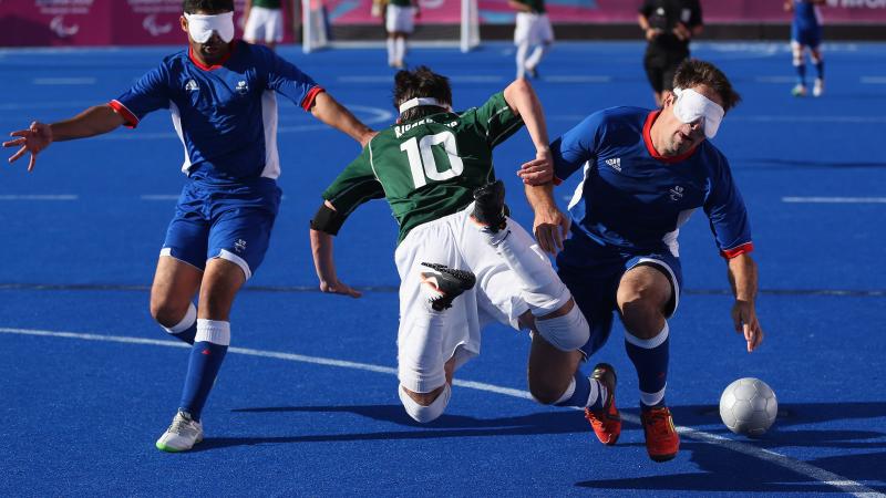 three blind football players go for the ball