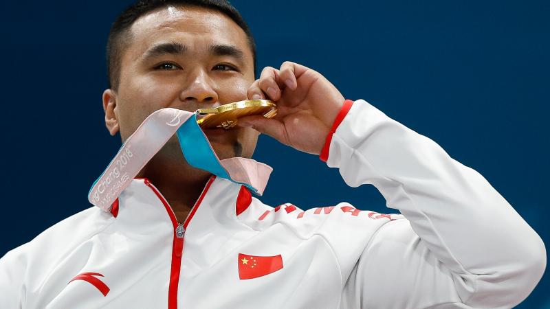 a male curler bites his gold medal