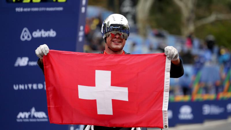 a male wheelchair racer holds up the Swiss flag