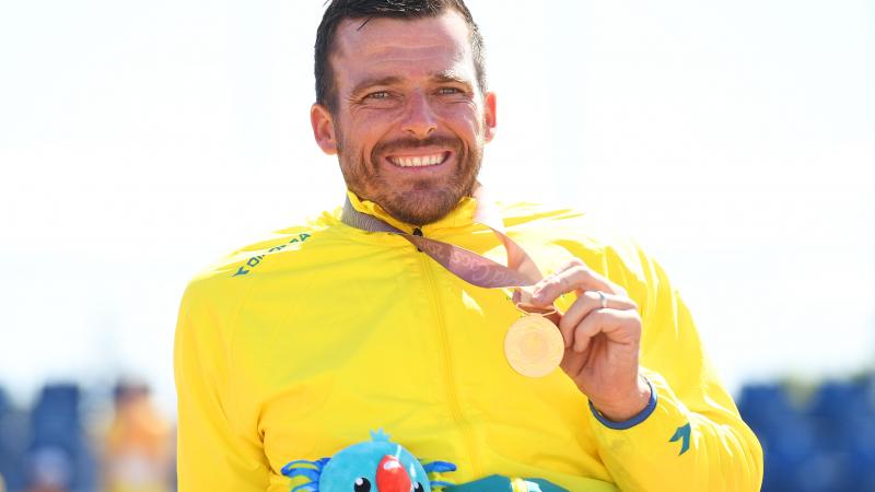 a male wheelchair racer holds up a gold medal