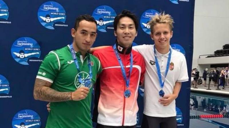 Three swimmers posing in front of a banner