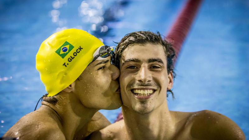 one male swimmer kissing another on the cheek in celebration