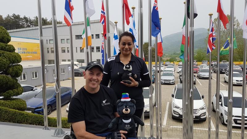 a male Para athlete and a woman standing both holding mascots