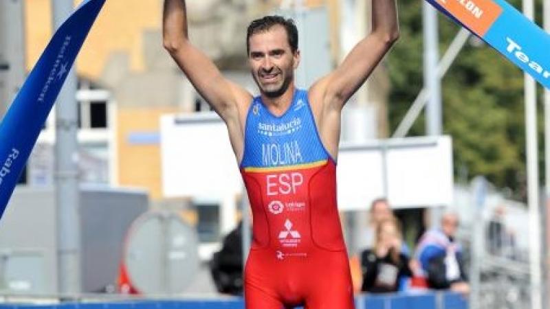 a male Para triathlete holds up the finish line tape as he crosses