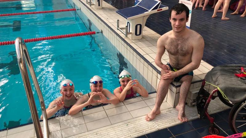 Three swimmers in the pool and one swimmer out of the pool posing for a picture