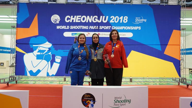 Three female shooting athletes pose on the podium