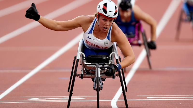 a female wheelchair racer punches the air as she crosses the line