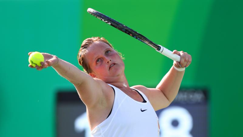 a female wheelchair tennis player prepares to serve