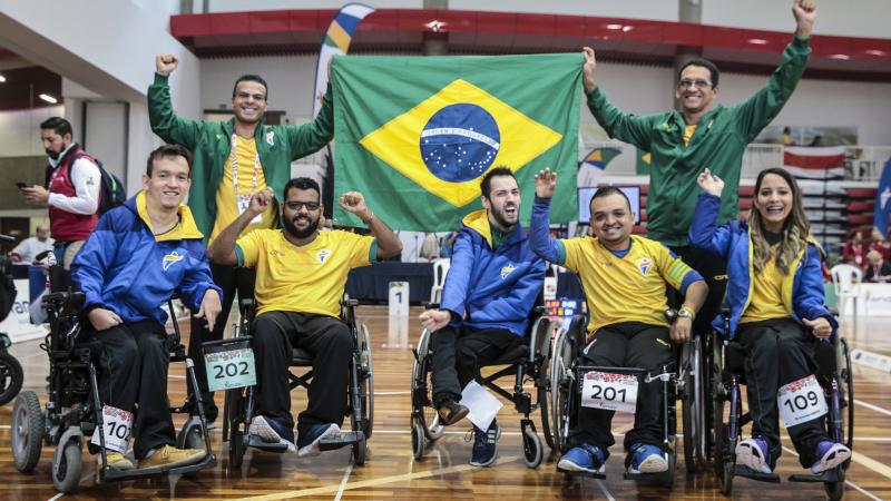 a group of boccia players wave their arms and hold up a Brazil flag