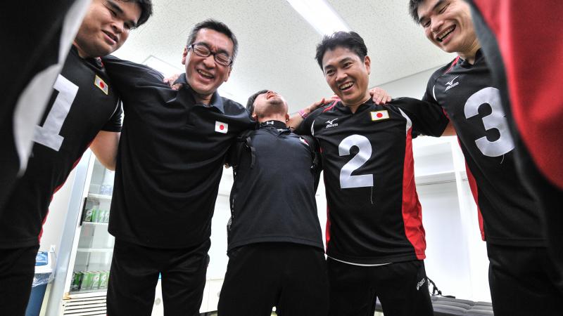 a group of male goalball players standing in a circle laughing 