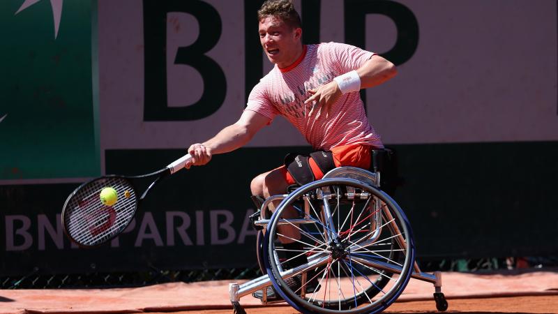 a male wheelchair tennis player reaches for a shot on a clay court