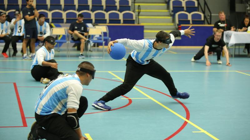 a male goalball player prepares to take a shot while two others wait beside him