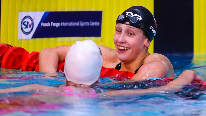 a female Para swimmer leans on the rope and chats to another swimmer