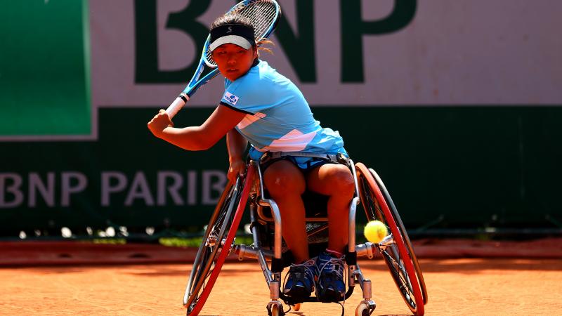 a female wheelchair tennis player plays a backhand shot