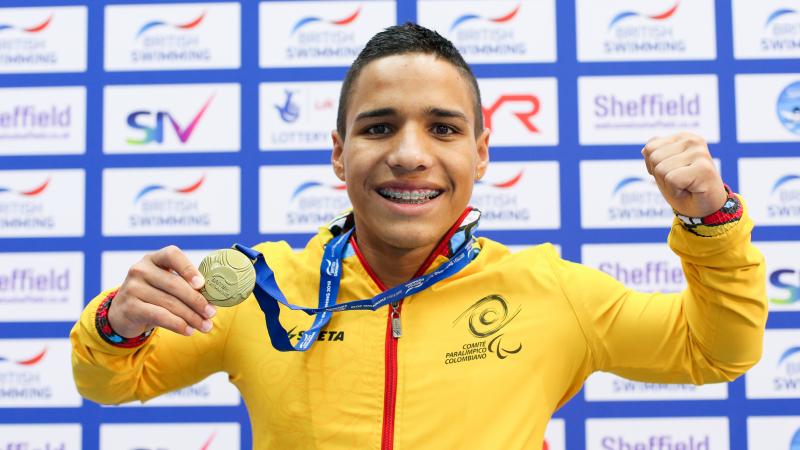 a male Para swimmer holds up his gold medal and smiles