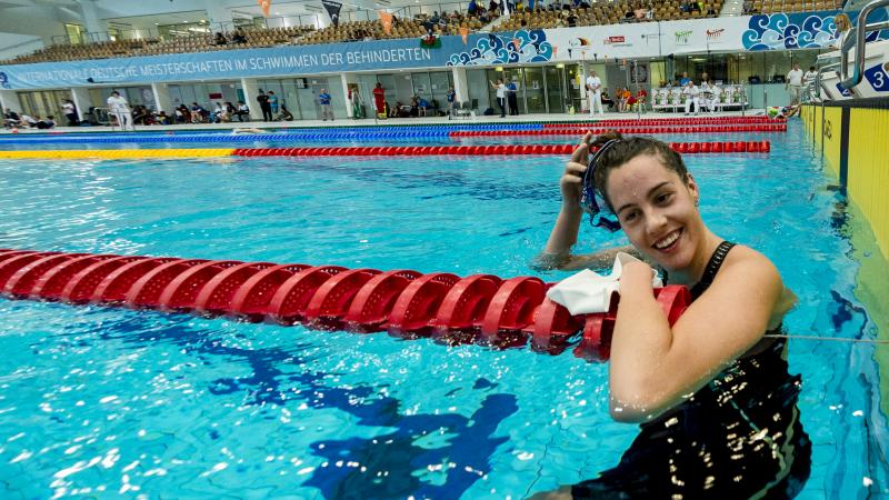 a female Para swimmer smiles in the water as she removes her swimming cap