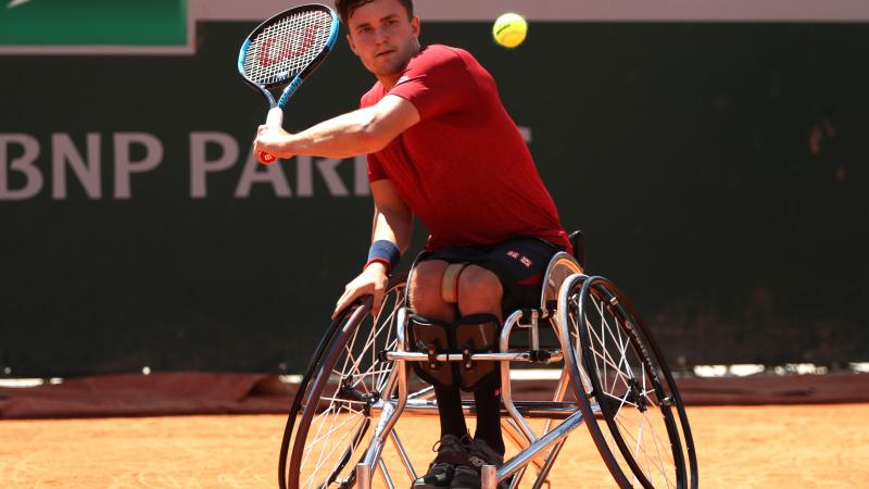 a male wheelchair tennis player plays a backhand on a clay court