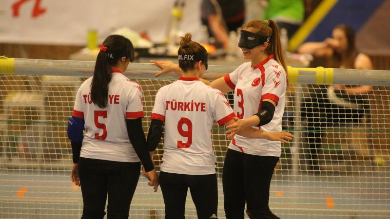 three female goalball players hug in celebration in front of the goal