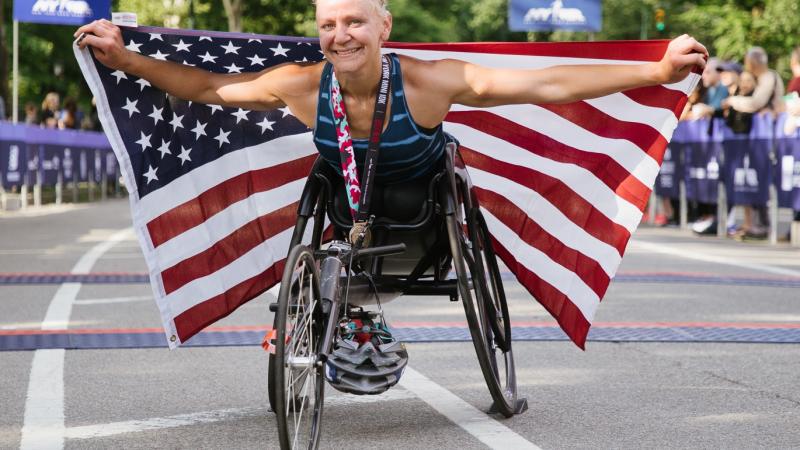 A female wheelchair racer holds up an American flag