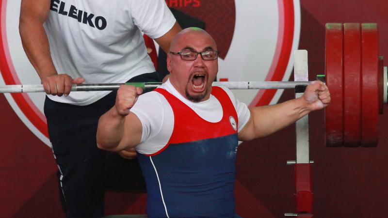 a male powerlifter raises his fists in celebration on the bench