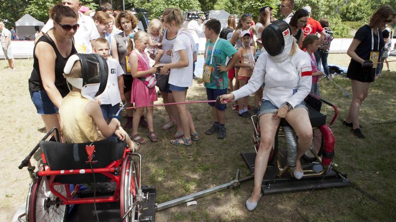 Group of children watching two people practicing wheelchair fencing