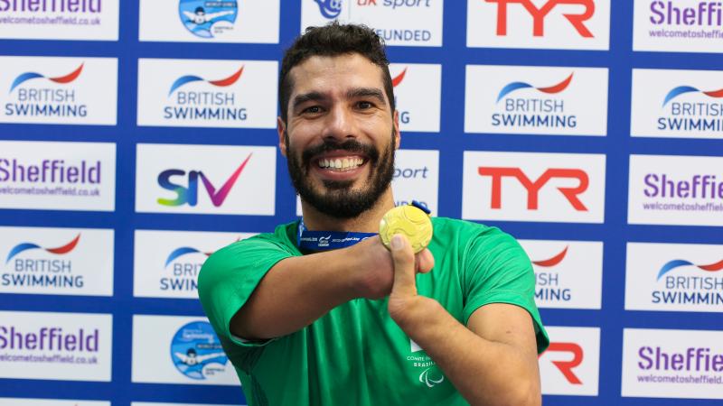 a male Para swimmer smiles and holds up his gold medal