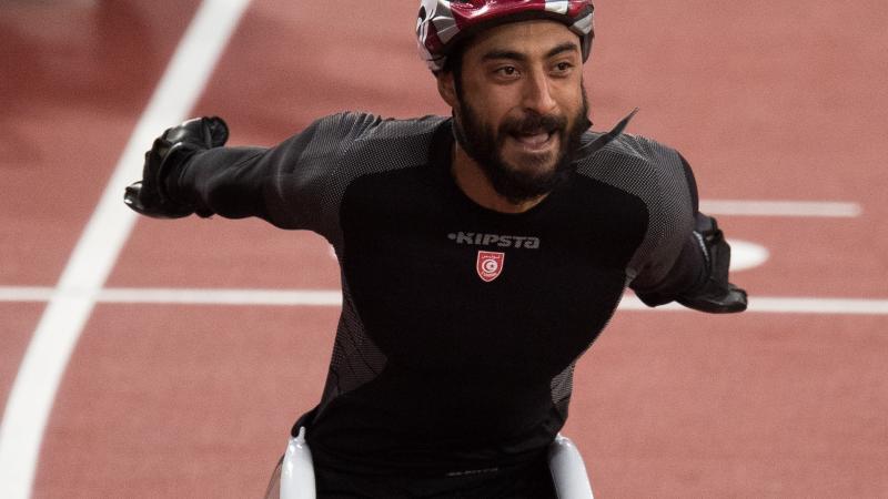 a male wheelchair racer throws his arms up in celebration