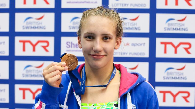 a female Para swimmer holds up a medal and smiles