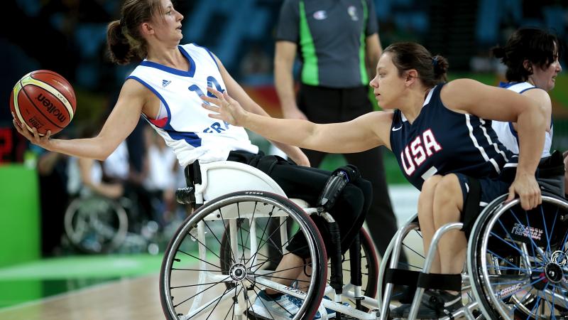 Woman in wheelchair holding a basketball while another tries to defend her