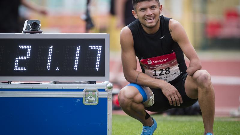 a male Para sprinter stands next to a race clock