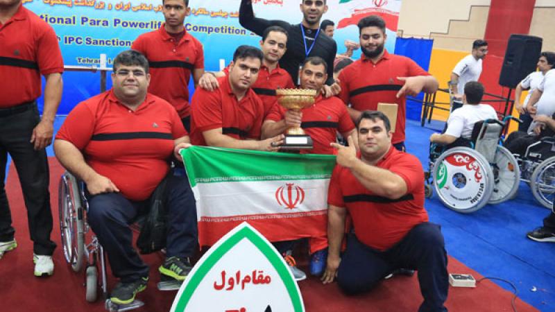 a group of male powerlifters holding an Iran flag and a trophy