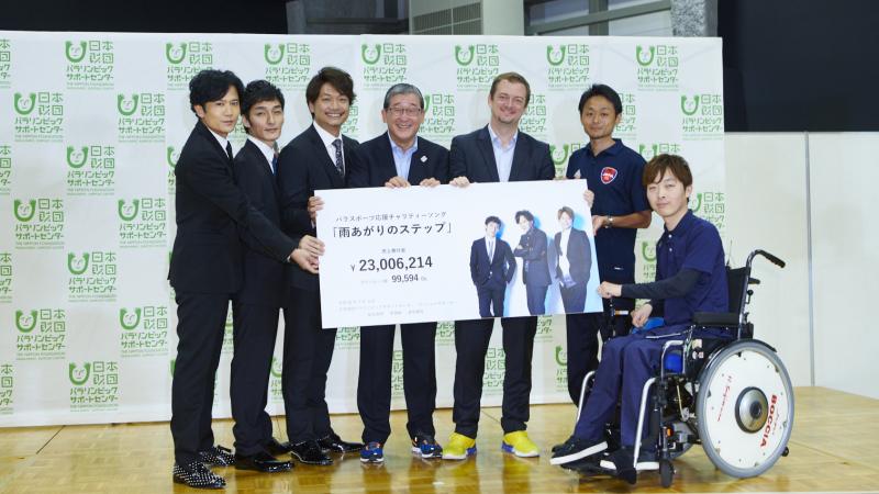 Six men standing and one in a wheelchair holding a cheque 