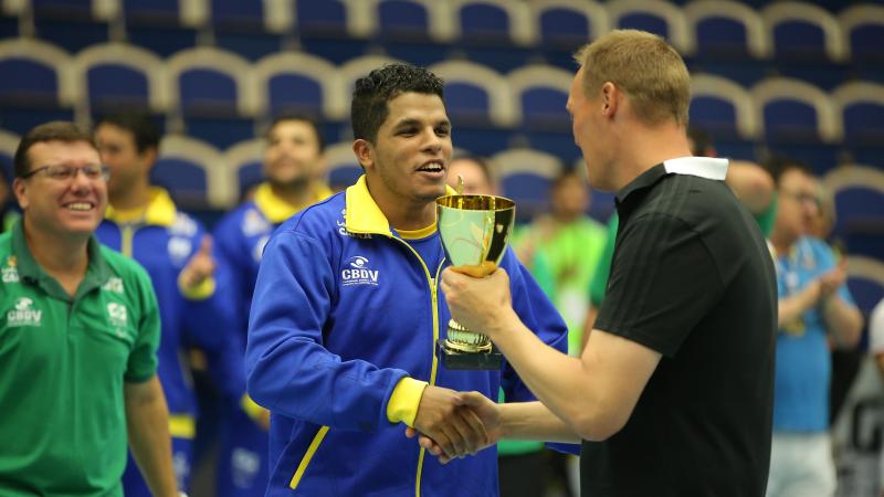 male goalballer player Leomon Moreno receives a trophy and shakes hands with another man