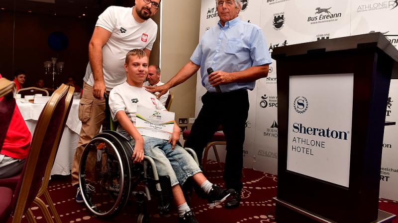 Polish male swimmer Juliusz Trochimczuk in a wheelchair receives an award from two men