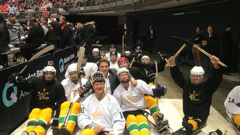 Fifteen people on sledges with Para ice hockey gear posing for a picture