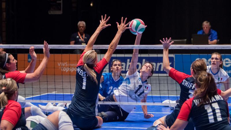 a group of female sitting volleyballers blocking the ball at the net 