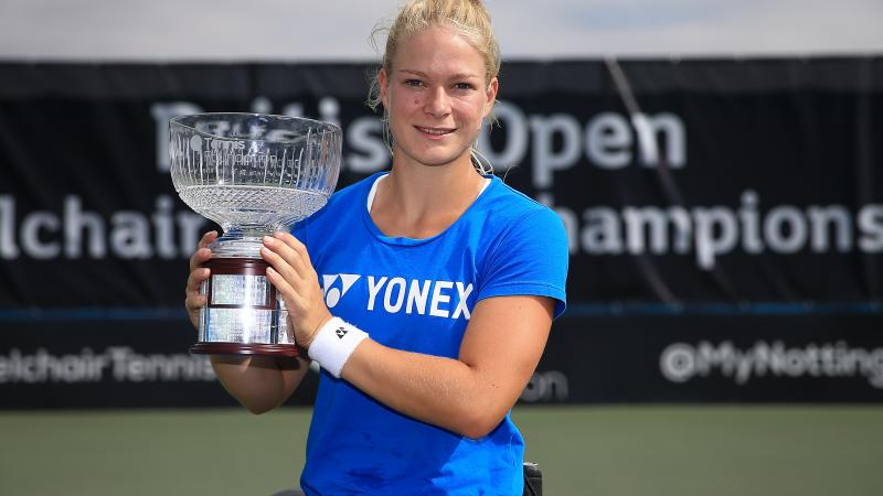 Female wheelchair tennis player Diede de Groot smiles and lifts a glass trophy