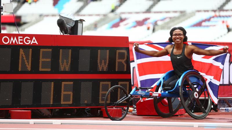 Female wheelchair racer Kare Adenegan holds up a British flag next to the display of her world record time