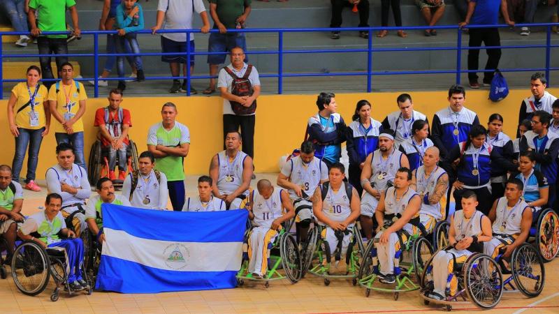 Nicaragua's wheelchair basketball players on a court holding up the Nicaragua flag