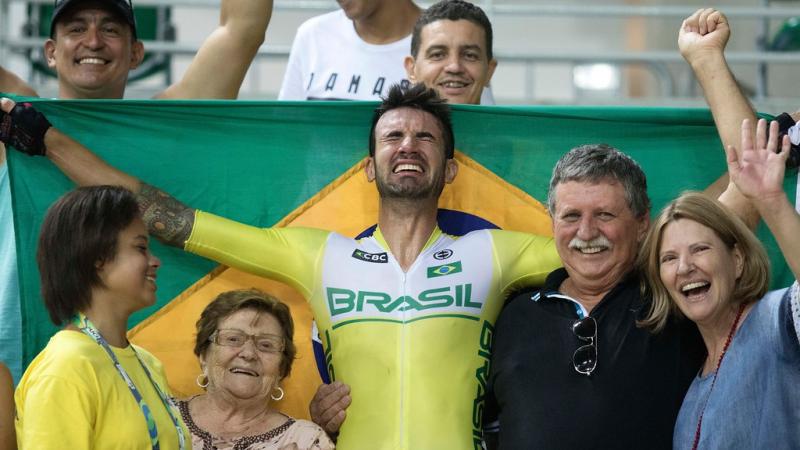 male Para cyclist Lauro Chaman celebrates with his family and holds up the Brazil flag