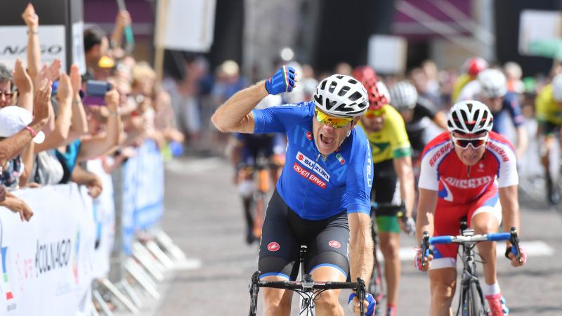 male Para cyclist Michele Pittacolo punches the air as he crosses the finish line