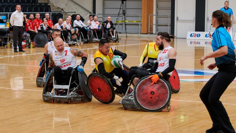 two Colombian wheelchair rugby players tackling a Polish player for the ball