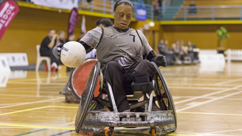 Woman in wheelchair rugby chair secures the ball with right hand